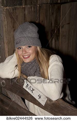 Smiling young woman wearing a hat and scarf standing at the gate of a horse's stall View Large Photo Image Stock Photograph - Smiling young woman wearing a hat and scarf standing at the gate of a horse's stall. Fotosearch