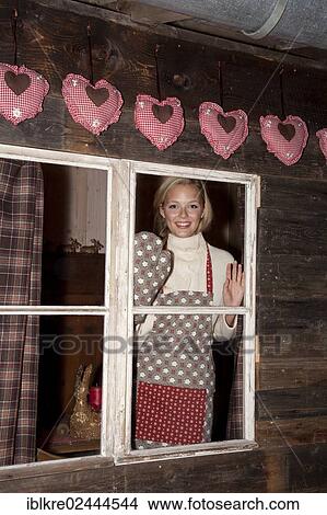 Smiling young woman wearing an apron standing at the window of a hiking hut View Large Photo Image Picture - Smiling young woman wearing an apron standing at the window of a hiking hut. Fotosearch