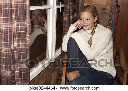 Smiling young woman with braids sitting at the window of a hiking hut and looking out View Large Photo Image Stock Photo - Smiling young woman with braids sitting at the window of a hiking hut and looking out. Fotosearch