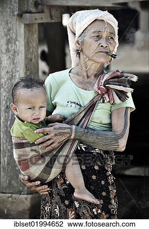 "Smoking grandmother carrying her grandchildren in a sling in a village on the Mekong, Laos, Southeast Asia, Asia" View Large Photo Image Stock Image - "Smoking grandmother carrying her grandchildren in a sling in a village on the Mekong, Laos, Southeast Asia, Asia". Fotosearch