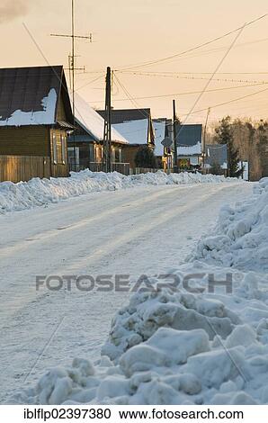 Stock Image - "Snow-covered road, traditional wooden houses and piles of cleared snow, Bialowieza Village, Podlaskie Voivodeship, Poland, Europe". Fotosearch