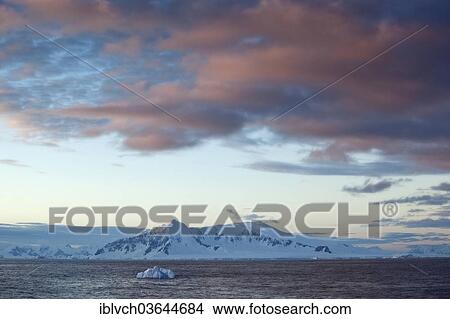 Picture - "Snow-covered rocks, first morning light, cloud atmosphere, Antarctic Peninsula, Antarctica". Fotosearch