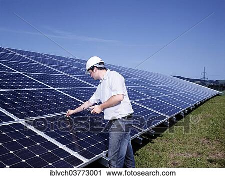 Stock Image - Solar installation technician checking solar panels with a measuring device. Fotosearch