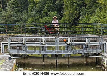 "Spectator with a bicycle observing a houseboat passing through a lock on the Canal des Vosges, formerly Canal de l'Est, Lock 33 at La Pipee, PK 124, Fontenoy-le-Chateau, Epinal, Lorraine, Departement Vosges, France, Europe" View Large Photo Image Stock Photograph - "Spectator with a bicycle observing a houseboat passing through a lock on the Canal des Vosges, formerly Canal de l'Est, Lock 33 at La Pipee, PK 124, Fontenoy-le-Chateau, Epinal, Lorraine, Departement Vosges, France, Europe". Fotosearch