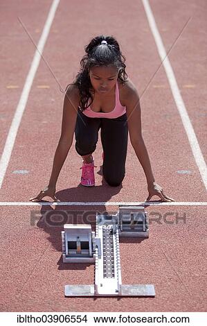 Picture - "Sporty young woman getting ready on running track, starting block". Fotosearch