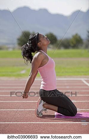 Stock Image - "Sporty young woman on running track, stretching arms". Fotosearch