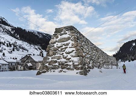 Stock Image - "Stone wall as protection against avalanches, behind wooden church, rear Paznauntal, Galtur, Tirol, Austria, Europe". Fotosearch