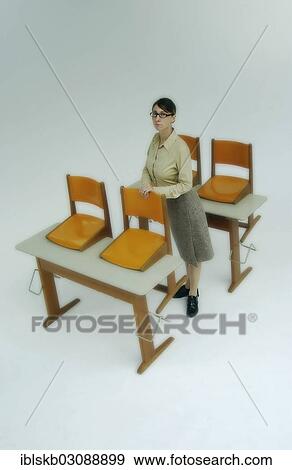 Strict Female Teacher Standing At Old School Desks With Orange