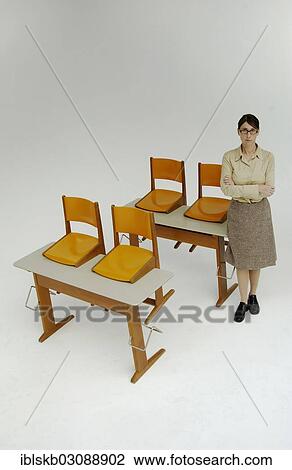 Strict Female Teacher Standing Next To Old School Desks With