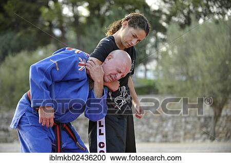 Stock Image - Student keeps her martial arts instructor in a headlock during a training session in a park. Fotosearch