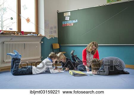 Stock Image - "Students at an independant school sitting and lying to work on the ground, Aktive Schule Peterhausen, Petershausen, Upper Bavaria, Bavaria, Germany, Europe". Fotosearch