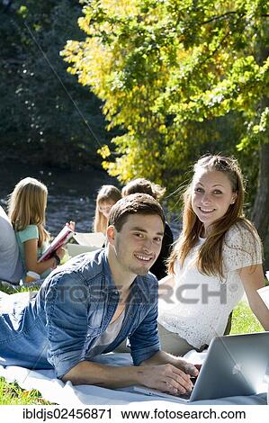 Stock Image - "Students with a laptop and books on a meadow, Freiburg im Breisgau, Baden-Wuerttemberg, Germany, Europe". Fotosearch