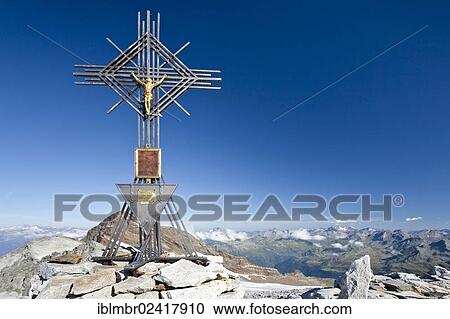 Stock Image - Summit cross on Magerstein mountain, Fernerkoepfl mountain and Schneebiger Nock mountain at the back, province of Bolzano-Bozen, Italy, Europe. Fotosearch