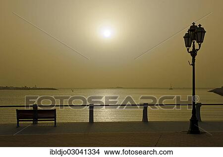 "Sun setting over the Persian Gulf behind a bench and a street lamp at the Corniche, Abu Dhabi, United Arab Emirates, Asia" View Large Photo Image Picture - "Sun setting over the Persian Gulf behind a bench and a street lamp at the Corniche, Abu Dhabi, United Arab Emirates, Asia". Fotosearch