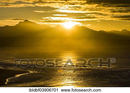 Stock Image - "Sunrise on the coast of the Indian Ocean, reflections of sun rays in the water, mountain ridge, Plettenberg Bay or Plettenbergbaai, Garden Route, Eden District, Western Cape, South Africa, Africa". Fotosearch