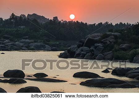 Stock Image - "Sunset over Tungabhadra river and a part of the ruins of the former Vijayanagara Empire, Hampi, Karnataka, India, Asia". Fotosearch