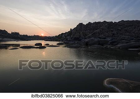 Stock Photograph - "Sunset over Tungabhadra river and a part of the ruins of the former Vijayanagara Empire, Hampi, Karnataka, India, Asia". Fotosearch