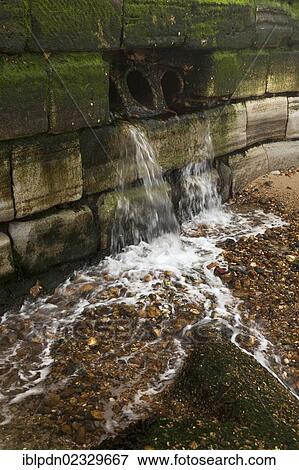 Surface water outlet in sea wall falling onto beach View Large Photo Image Stock Photo - Surface water outlet in sea wall falling onto beach. Fotosearch