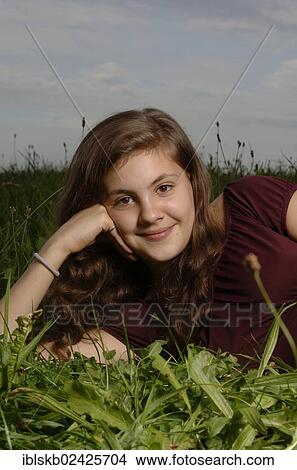 Picture - "Teenage girl lying on the grass, supporting her head on her hand and smiling". Fotosearch