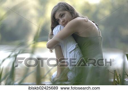 Stock Photo - "Teenage girl sitting amidst reeds by a lake, dreaming". Fotosearch