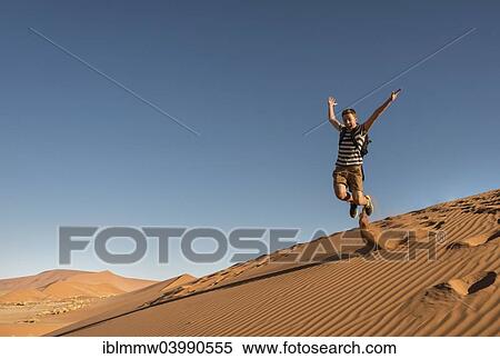 Stock Photography - "Teenager jumping and running down a dune, Sossusvlei, Namib Desert, Namibia, Africa". Fotosearch