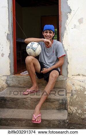 "Teenager with football sitting in front of his home in a favela, Poxoreo, Mato Grosso, Brazil, South America" View Large Photo Image Picture - "Teenager with football sitting in front of his home in a favela, Poxoreo, Mato Grosso, Brazil, South America". Fotosearch
