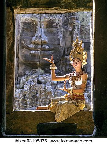 Stock Photograph - "Temple dancer or apsara sitting in a window in front of a face tower at Bayon Temple, UNESCO World Cultural Heritage Site, Angkor Thom, Siem Reap, Siem Reap Province, Cambodia, Asia". Fotosearch