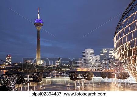 "Terrace of a restaurant, Gehry buildings at dusk at the back, Neuer Zollhof building complex and the Rheinturm tower, Medienhafen district, Duesseldorf, North Rhine-Westphalia, Germany, Europe" View Large Photo Image Stock Photo - "Terrace of a restaurant, Gehry buildings at dusk at the back, Neuer Zollhof building complex and the Rheinturm tower, Medienhafen district, Duesseldorf, North Rhine-Westphalia, Germany, Europe". Fotosearch