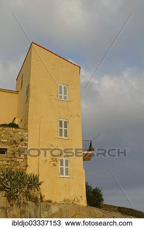 "The facade of a yellow house with windows and a balcony in the citadel of Calvi below a cloudy sky. Calvi is in the department Haute-Corse, France on the mediterranean island of Corsica, Calvi, Corsica, France, Europe" View Large Photo Image Stock Image - "The facade of a yellow house with windows and a balcony in the citadel of Calvi below a cloudy sky. Calvi is in the department Haute-Corse, France on the mediterranean island of Corsica, Calvi, Corsica, France, Europe". Fotosearch