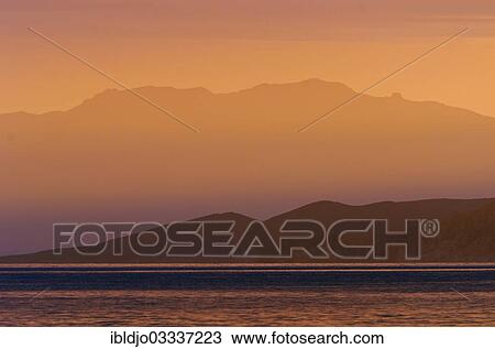 Stock Image - "The rising sun forms sun beams behind the rocks of the island Ile de la Pietra near L'Ile-Rousse. L'Ile-Rousse is in the department Haute-Corse, France on the mediterranean island of Corsica, Ile de la Pietra, Lâ€™Ile-Rousse, Corsica, France, Europe". Fotosearch