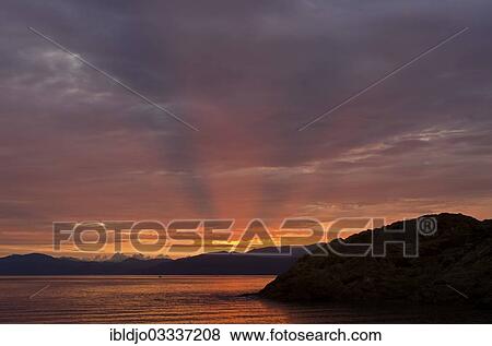 Stock Photo - "The rising sun forms sun beams behind the rocks of the island Ile de la Pietra near L'Ile-Rousse. L'Ile-Rousse is in the department Haute-Corse, France on the mediterranean island of Corsica, Ile de la Pietra, Lâ€™Ile-Rousse, Corsica, France, Europe". Fotosearch