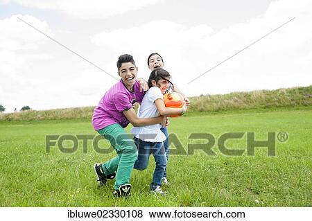 Three children playing ball on a meadow View Large Photo Image Stock Photo - Three children playing ball on a meadow. Fotosearch