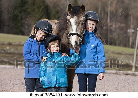 "Three children wearing riding helmets standing beside a pony, dun, with a bridle, Tyrol, Austria, Europe" View Large Photo Image Stock Image - "Three children wearing riding helmets standing beside a pony, dun, with a bridle, Tyrol, Austria, Europe". Fotosearch