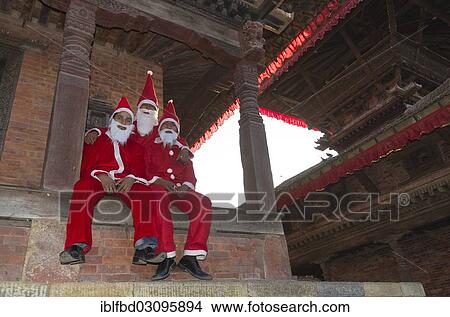 Picture - "Three local men costumed as Santa Claus sitting on temple steps at Durbar Square, Kathmandu Valley, Kathmandu, Kathmandu District, Bagmati Zone, Nepal, Asia". Fotosearch