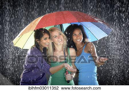 "Three smiling young women of Cuban, Indian and German descent, standing together under a colourful rainbow umbrella enjoying the rain" View Large Photo Image Stock Image - "Three smiling young women of Cuban, Indian and German descent, standing together under a colourful rainbow umbrella enjoying the rain". Fotosearch