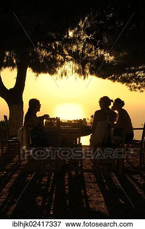 Three women sitting at a table in a seaside garden at sunset, Lefkas, Greece, Europe View Large Photo Image Stock Photo - Three women sitting at a table in a seaside garden at sunset, Lefkas, Greece, Europe. Fotosearch