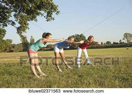 Three young women doing gymnastics exercises together in a meadow View Large Photo Image Stock Image - Three young women doing gymnastics exercises together in a meadow. Fotosearch
