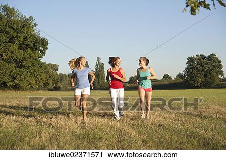 Three young women jogging together across a meadow View Large Photo Image Stock Image - Three young women jogging together across a meadow. Fotosearch