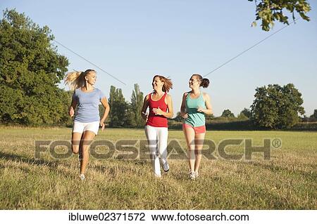 Stock Image - Three young women jogging together across a meadow. Fotosearch
