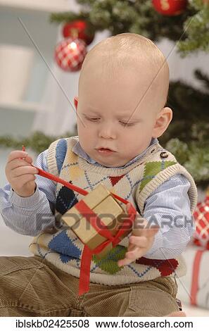 Toddler unwrapping a golden gift in front of a Christmas tree View Large Photo Image Stock Photo - Toddler unwrapping a golden gift in front of a Christmas tree. Fotosearch