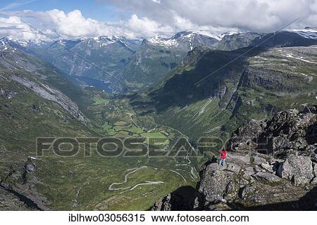 Stock Photography - "Tourist standing on a rock on Dalsnibba Mountain, 1495m, looking towards Geirangerfjord, Geiranger, Reichsstrasse 63, More og Romsdal, Western Norway, Norway, Europe". Fotosearch