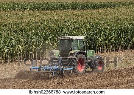 Stock Photo - "Tractor with a cultivator in front of a field of Corn (Zea mays subsp. Mays), Germany, Europe, PublicGround, Europe". Fotosearch