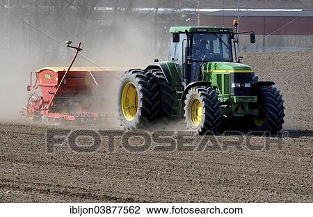 Stock Image - "Tractor with sowing machine works on dusty fields at spring farming. Kopingebro, Scania, Sweden, Europe". Fotosearch