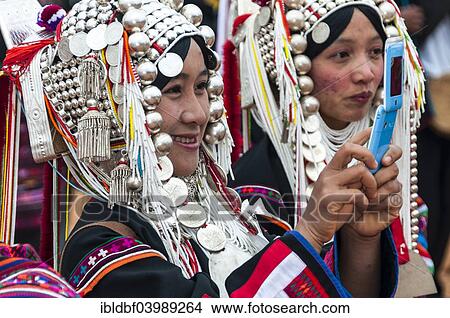 Picture - "Traditionally dressed smiling young woman from the Akha people, hill tribe, ethnic minority, taking a picture with a mobile phone, Chiang Rai Province, Northern Thailand, Thailand, Asia". Fotosearch