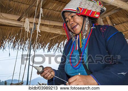Stock Image - "Traditionally dressed woman from the Akha people, hill tribe, ethnic minority, weaving yarn, Chiang Rai Province, Northern Thailand, Thailand, Asia". Fotosearch