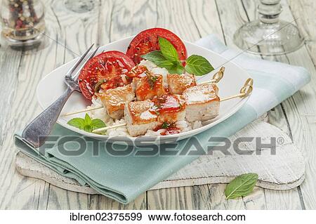 Stock Photo - Turkey skewers on rice with tomato sauce and grilled tomatoes. Fotosearch