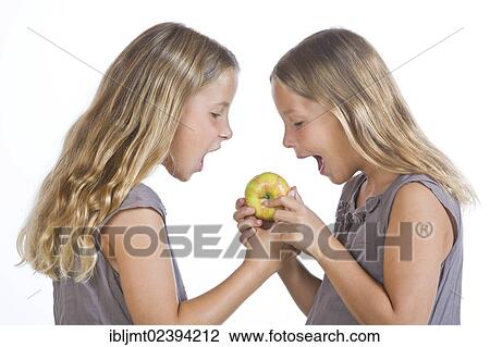 Stock Image - "Twin girls, 9, biting into an apple". Fotosearch