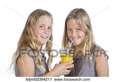 Stock Image - "Twin girls, 9, drinking orange juice together". Fotosearch