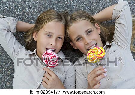 "Twin girls, 9, lying on the floor with colourful lollipops" View Large Photo Image Stock Photo - "Twin girls, 9, lying on the floor with colourful lollipops". Fotosearch