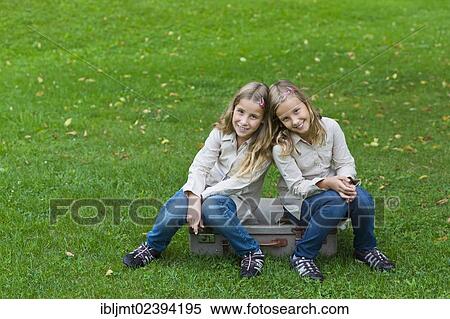Stock Photography - "Twin girls, 9, sitting on a suitcase in the grass". Fotosearch
